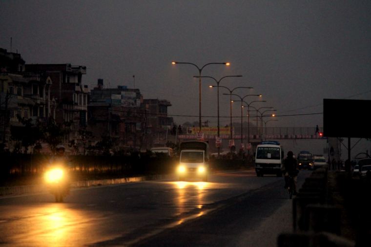 Headlights on a wet road at dusk with street lamps